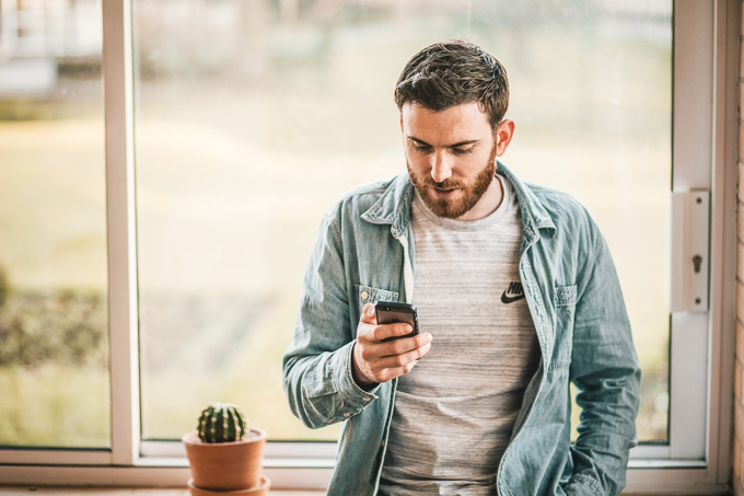 Junger Mann blickt auf sein Smartphone in der Hand